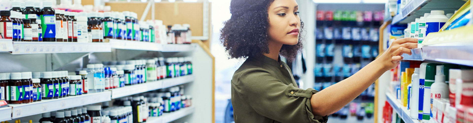Banner featuring young black woman selecting products off of retail pharmacy aisle of medications